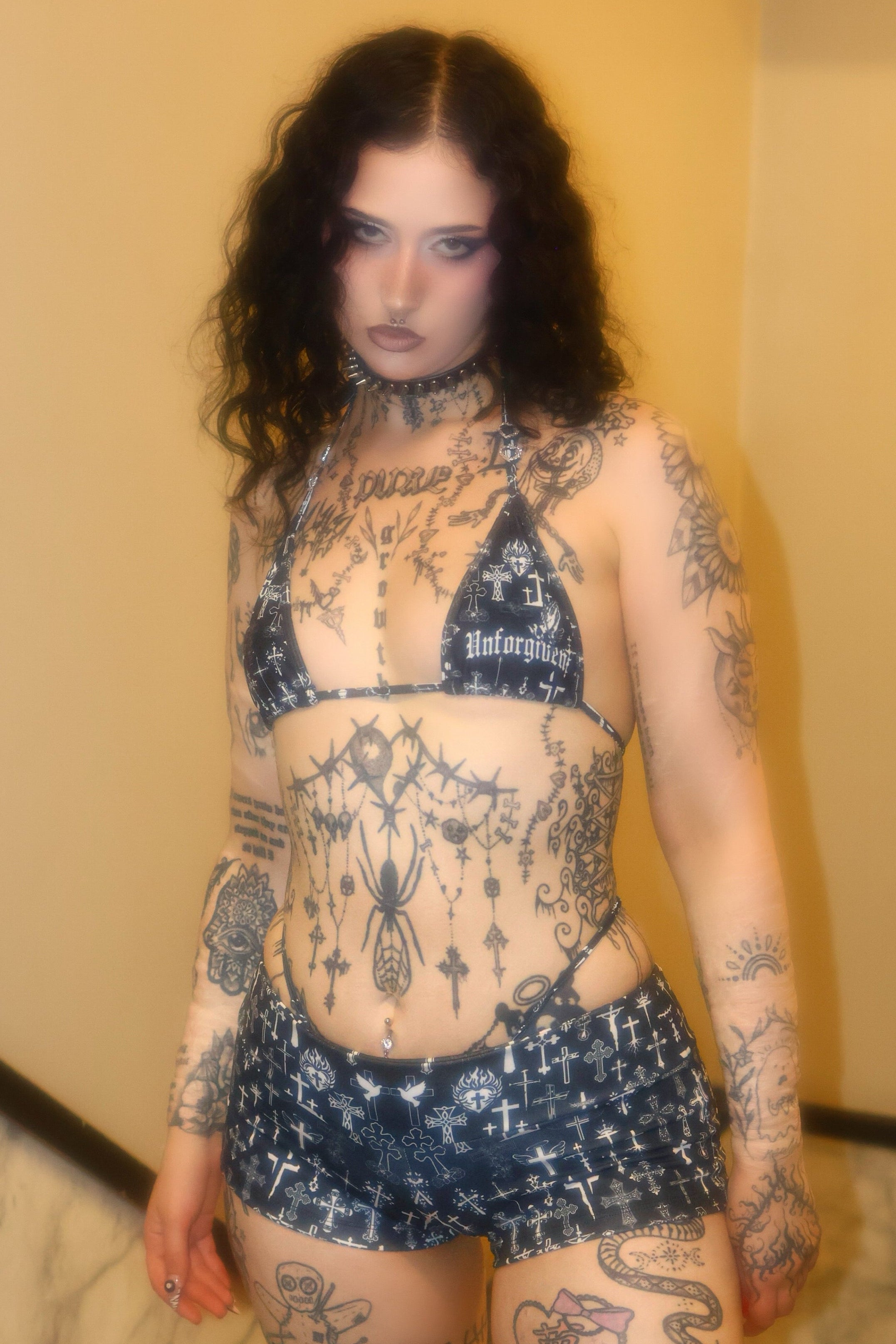 Person with extensive tattoos wearing a black and white outfit indoors.